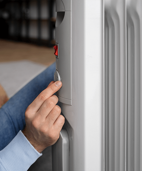 Radiateur électrique : réglage chauffage et économies Main réglant le thermostat d'un radiateur électrique gris. Un interrupteur rouge est visible, suggérant le chauffage domestique.